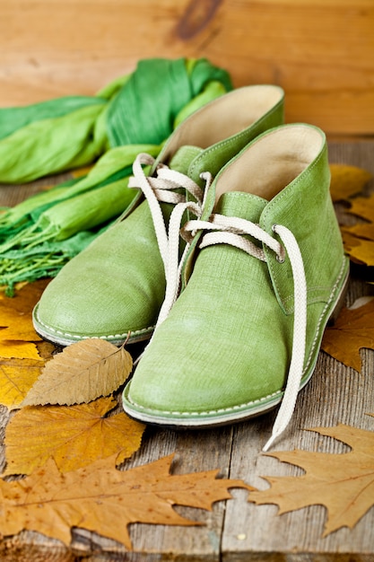 Botas de couro verde, cachecol e folhas amarelas