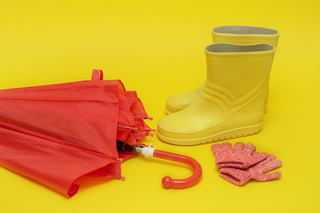 Botas e luvas de guarda-chuva para crianças vermelhas em um fundo amarelo com espaço de cópia