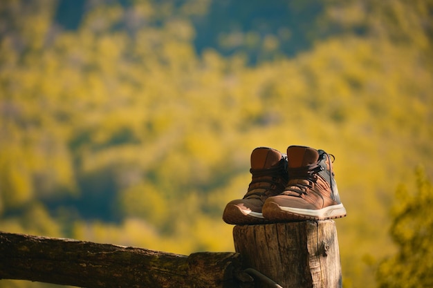 Botas de un excursionista apoyado en un poste con una montaña al fondo después de una excursión