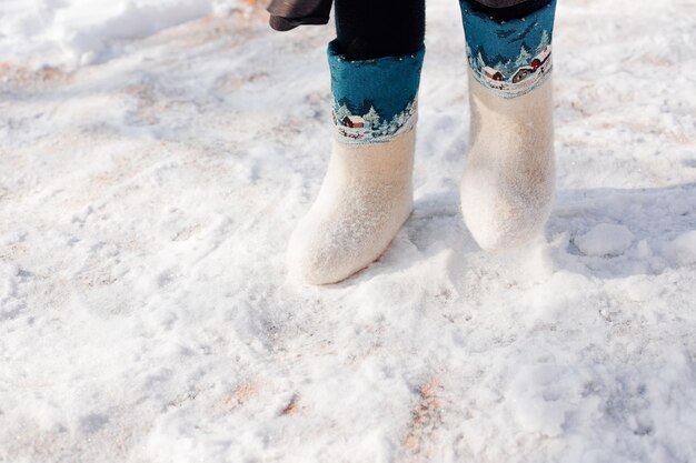 Botas de fieltro blanco con adorno de cerca de los pies del hombre calzados en botas de fieltro y de pie sobre la nieve fresca que ...