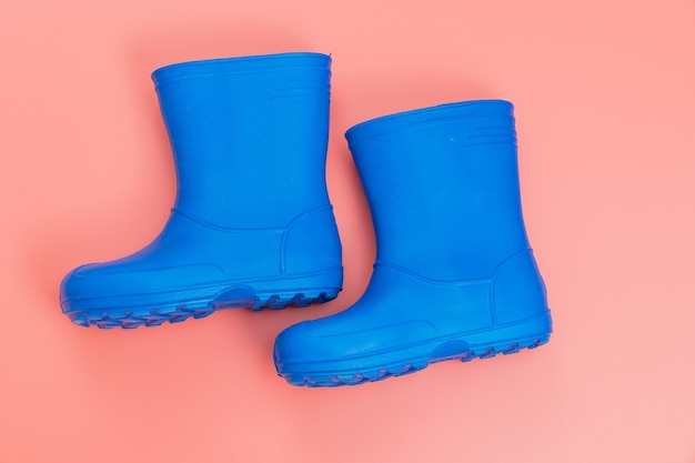 Botas de goma azul sobre fondo rosa. zapatos para lluvia y charcos. zapatería. proteja sus pies de la humedad y la suciedad.