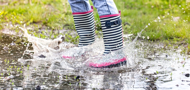 Botas de goma en un charco en el proceso de saltar con salpicaduras de agua de cerca.