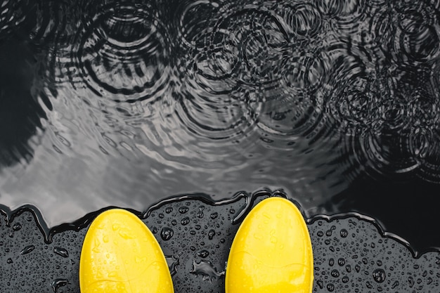 Botas de goma de color amarillo brillante de pie bajo la lluvia sobre negro