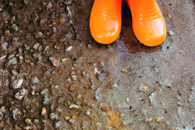 Botas de goma naranjas de pie junto al charco.
