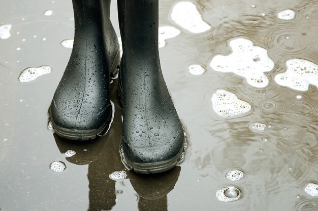 Foto botas de goma negra en un charco sobre una carretera asfaltada en la ciudad en otoño el tiempo lluvioso en la ciudad