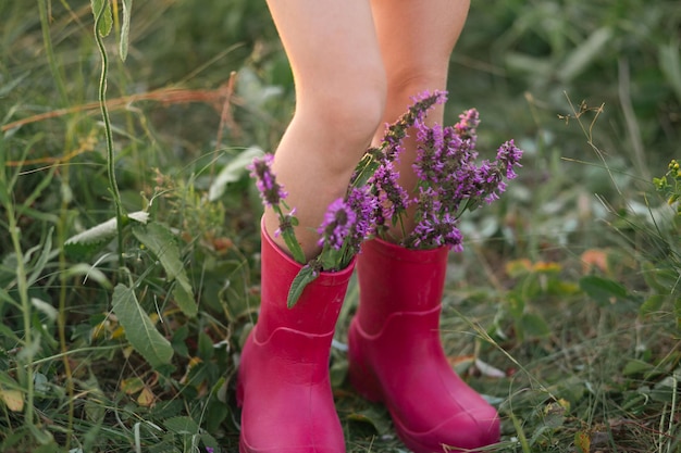 Botas de goma roja en los pies de una niña con un ramo de flores silvestres Flores en una bota verano verano libertad naturaleza campo verde hierba en el campo