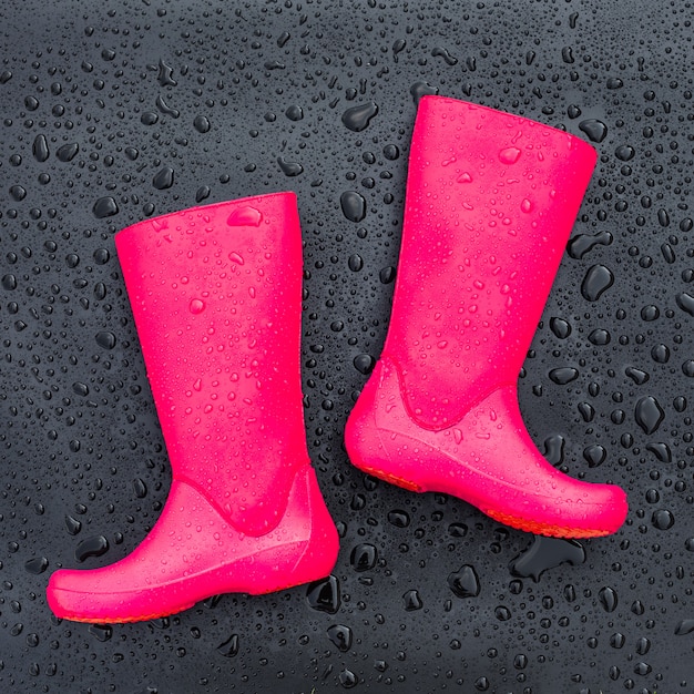 Botas de goma rosa brillante de moda en superficie mojada negra cubierta con gotas de lluvia