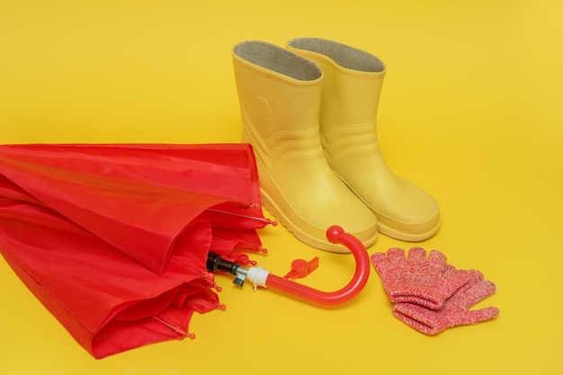 botas y guantes de paraguas rojos para niños sobre un fondo amarillo con espacio de copia