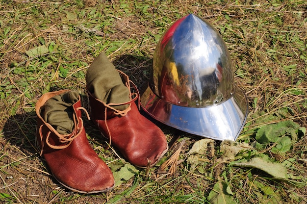 Botas medievales teutónicas y casco tirado en el suelo.