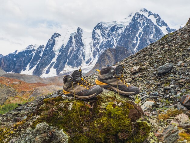 Botas de montaña mojadas se secan sobre una piedra con el telón de fondo de altas montañas cubiertas de nieve. Las dificultades del senderismo, secar la ropa en la naturaleza.