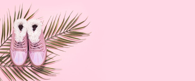 Botas para uma menina uma folha de uma palmeira em um fundo rosa Vista superior plana lay Banner