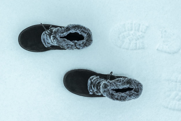 Botas de piel de mujer abrigadas caminando en la nieve. La vista desde arriba. Preciosos y prácticos zapatos de invierno para mujer.