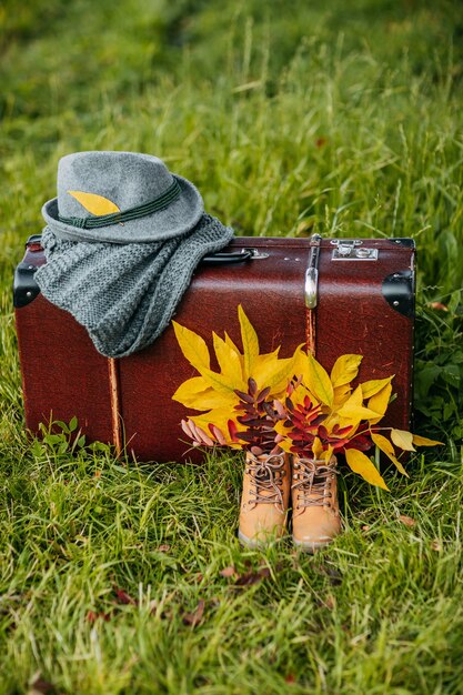 Botas viejas, sombrero de fieltro y bufanda tejida con la maleta vintage marrón en el bosque de otoño