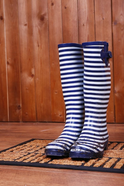 Botas Wellington sucias en la alfombra de la puerta en la habitación