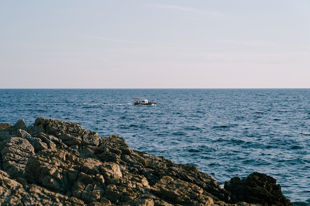 Un bote a motor con un toldo y los turistas montan las olas en el mar cerca de la costa rocosa