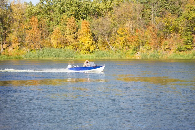 Un bote pequeño flota en el río de otoño. Pescadores navegar en un barco