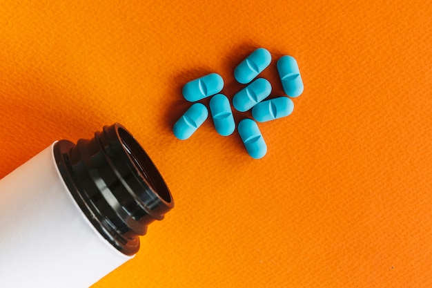 Foto botella abierta cerca de pastillas azules sobre fondo naranja