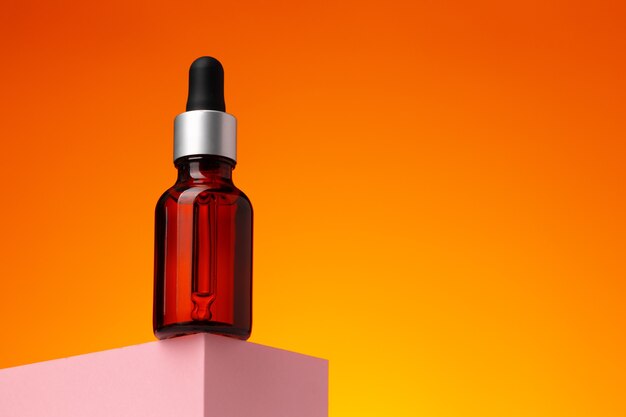 Botella de aceite de belleza con pipeta contra la superficie naranja