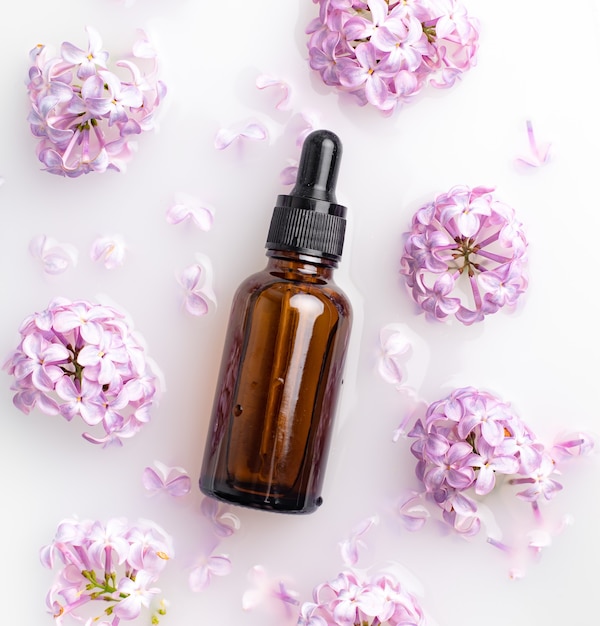 Una botella de aceite cosmético y ramas de lilas Cosmetología Aceite cosmético para la piel