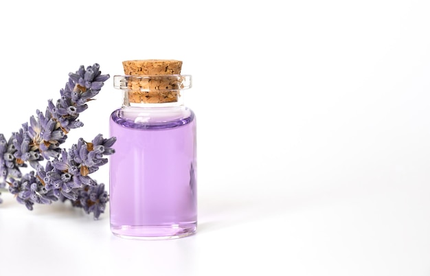 Botella de aceite esencial y flores de lavanda sobre fondo blanco.