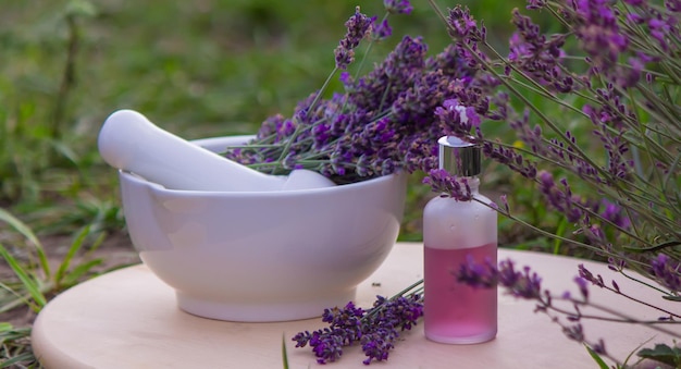 Botella de aceite esencial de lavanda sobre mesa de madera y fondo de campo de flores