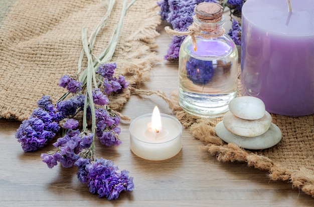 Botella con aceite esencial de lavanda, vela en mesa de madera.