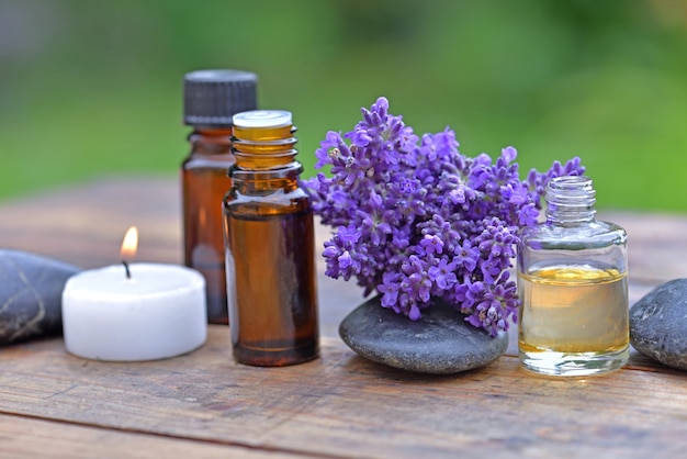 Botella de aceite esencial y ramo de flores de lavanda dispuestas sobre una mesa de madera con una vela