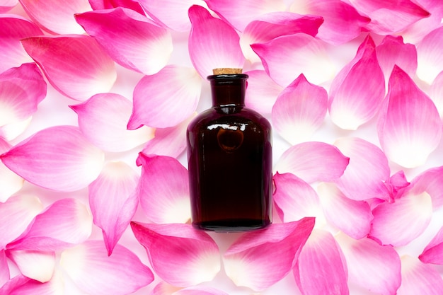 Botella de aceite esencial sobre fondo de pétalos de loto rosa.