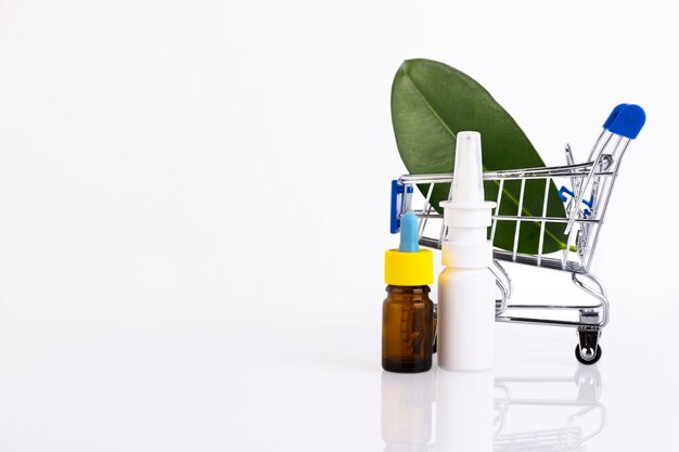 Botella de aceite esencial de vidrio ámbar en blanco con pipeta, spray nasal sobre fondo de hojas verdes.