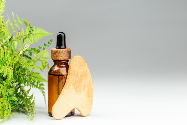 Botella de aceite y masajeador de madera gua sha sobre gris