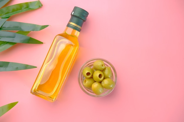 Botella de aceite de oliva y aceituna fresca en un recipiente en rosa