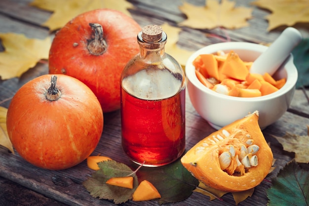 Botella de aceite de semillas de calabaza calabazas y mortero sobre mesa de madera con hojas de otoño Enfoque selectivo