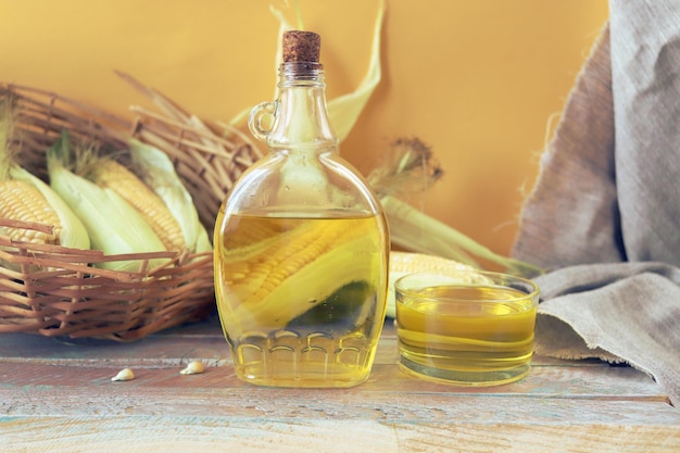 Una botella de aceite sobre la mesa, con el telón de fondo de maíz fresco con hojas, productos orgánicos