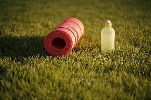 Botella de agua y colchoneta de ejercicios en el césped en el paseo marítimo