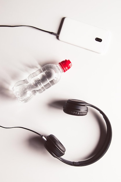 Botella de agua deportiva, auriculares y teléfono móvil sobre fondo blanco.