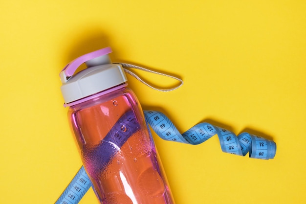 Botella de agua deportiva de plástico reutilizable y cinta métrica azul sobre fondo amarillo espacio de copia de vista superior