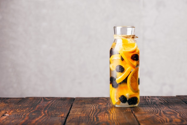 Botella de agua detox con infusión de naranja cruda en rodajas y mora fresca.