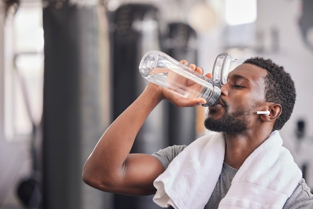 Botella de agua hombre negro cansado en el gimnasio y descansando después del ejercicio físico ejercicio deportivo saludable y entrenamiento de crecimiento muscular Motivación de descanso y atleta sediento bebiendo agua para el bienestar de la hidratación