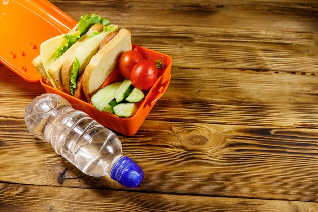 Botella de agua y lonchera con bocadillos y verduras frescas en una mesa de madera