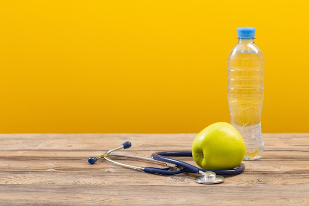 Botella de agua con manzana verde y estetoscopio sobre mesa de madera