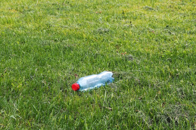 Una botella de agua de plástico con un tapón rojo descansa sobre un césped recién recortado. Concepto de tirar basura del medio ambiente.