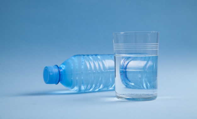 Botella de agua de plástico y vaso de agua en la pared azul,