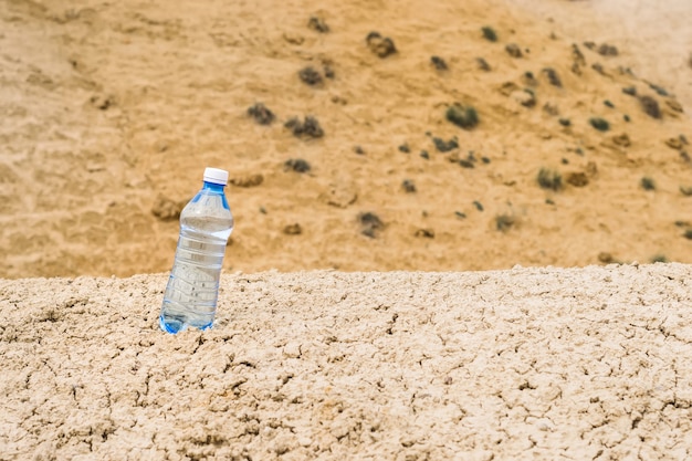 Botella de agua potable limpia en un desierto seco, espacio de copia
