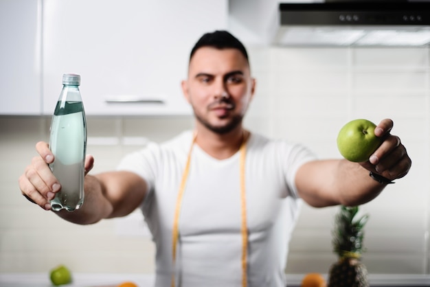 Botella de agua y un primer plano de manzana en manos de un hombre atlético en la cocina