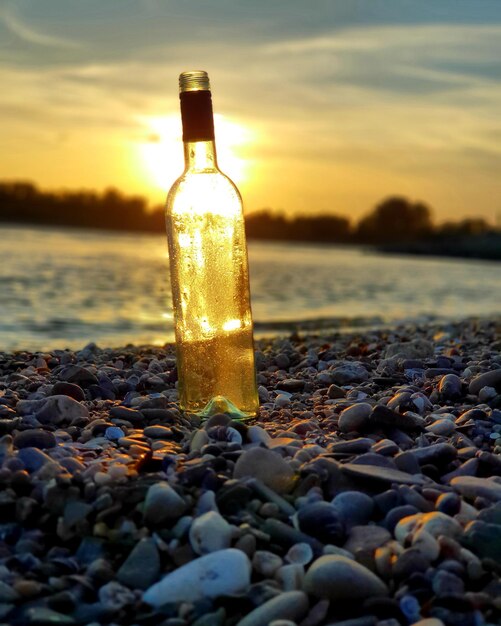 Foto botella de agua en las rocas en la playa durante la puesta de sol