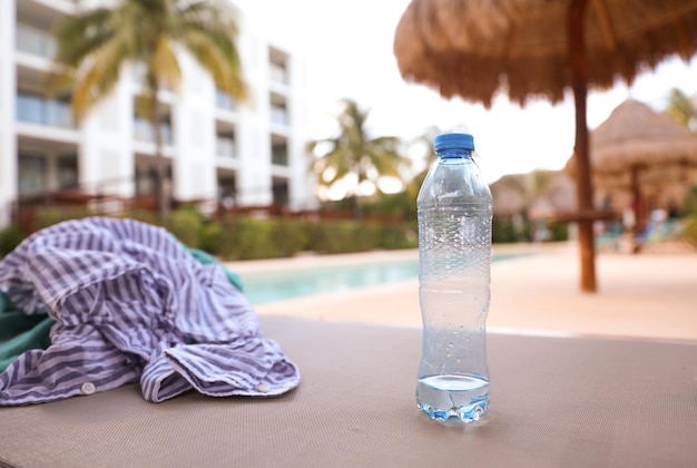 Una botella de agua se sienta en una mesa frente a una piscina.