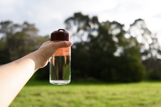 Una botella de agua sostenida por una mano femenina en el fondo de la naturaleza.