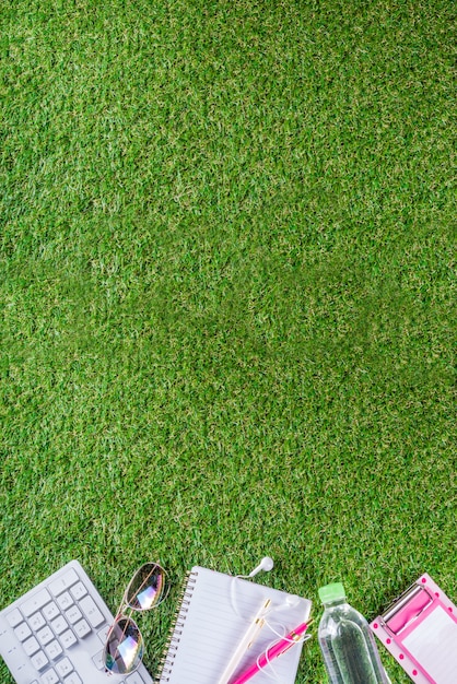 Botella de agua, teclado, cuaderno sobre hierba verde