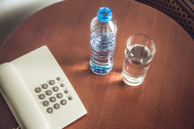 Botella de agua y vaso con teléfono en la mesa