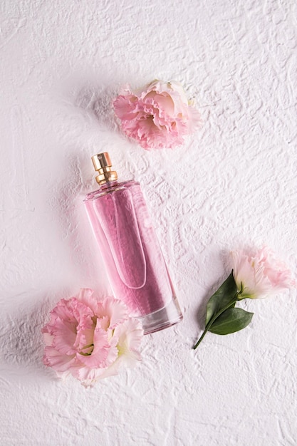 Una botella alta y elegante de perfume para mujeres sobre un fondo blanco con flores Vista vertical Presentación de la delicada fragancia del perfume